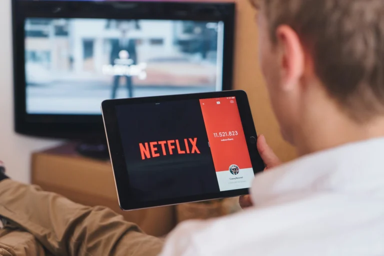 Persona con una tablet mirando netflix y un televisor de pantalla plana de fondo